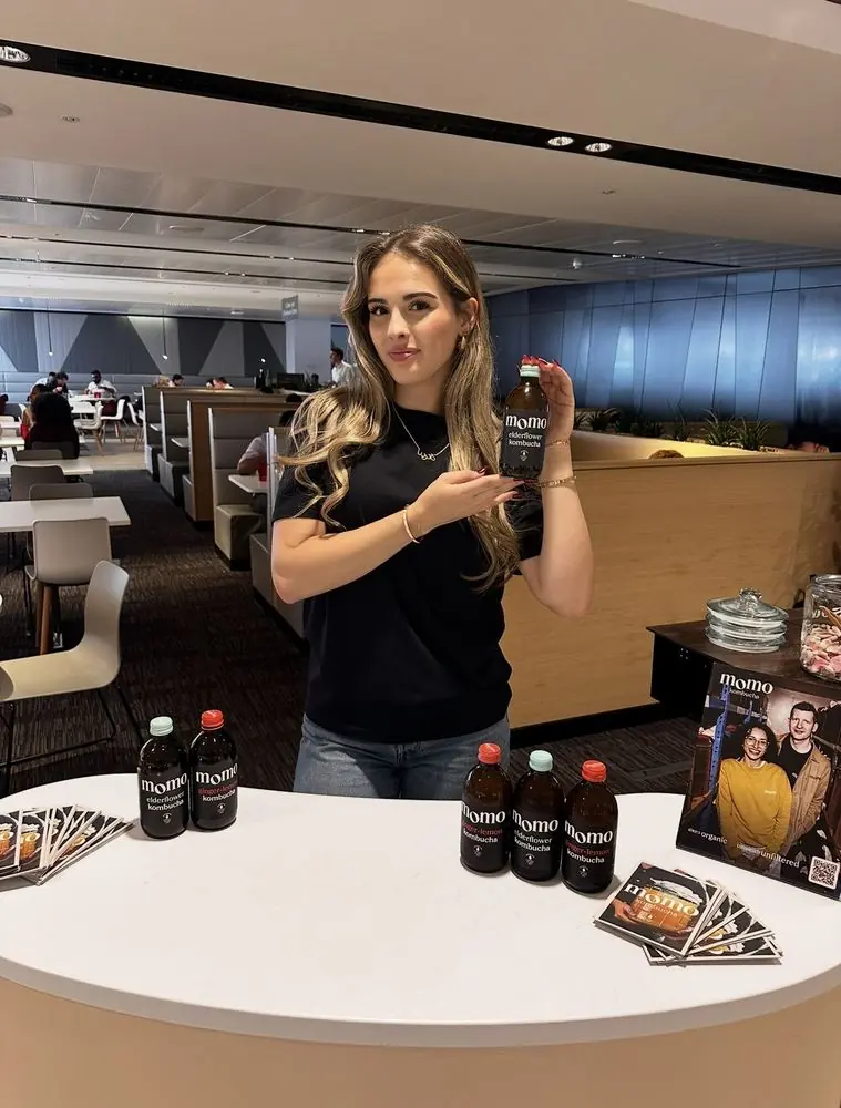 Katrina holding a bottle of Momo elderflower kombucha at a sampling table