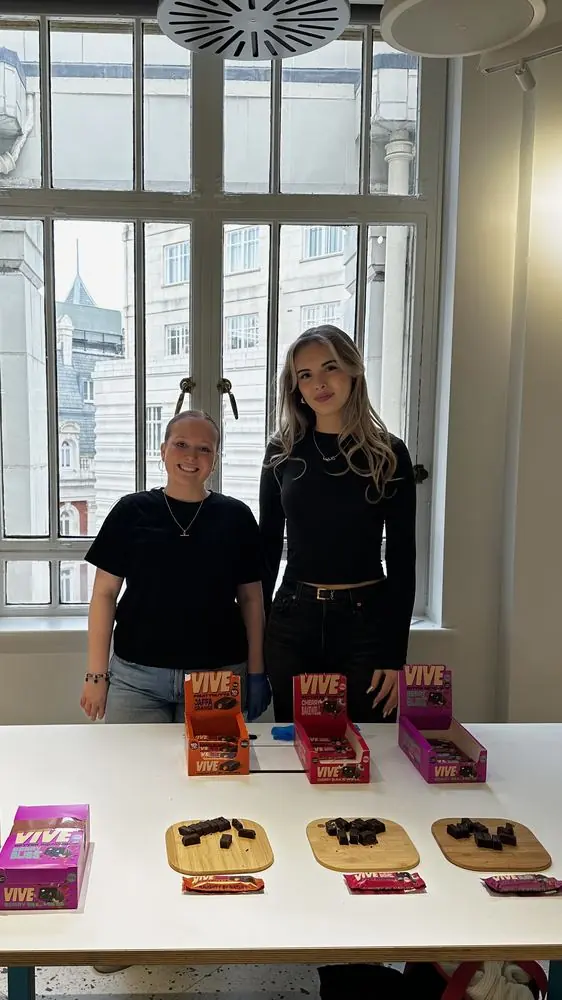 Two women behind a sampling table with Vive bars and tasting boards