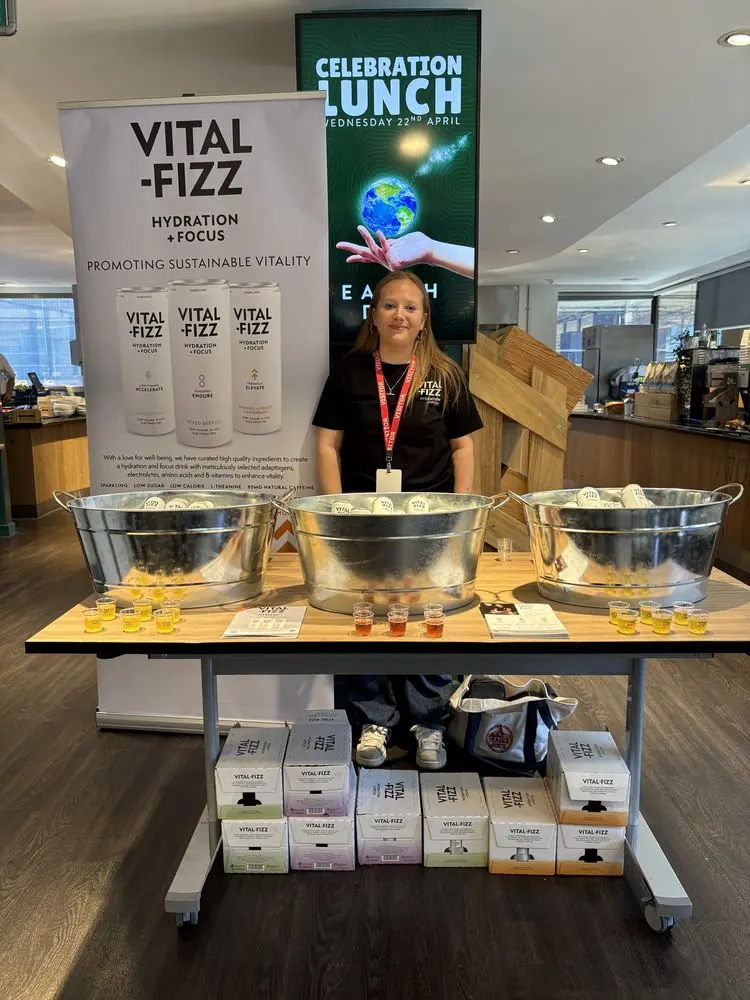 Sampling stand with ice buckets of drink samples in front of a Vital Fizz banner