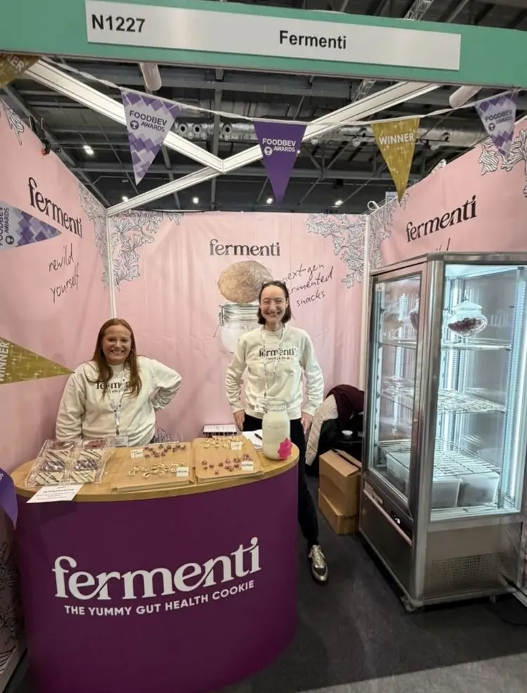 Two women at the Fermenti stand at a food and drink trade show, with cookie samples on the counter