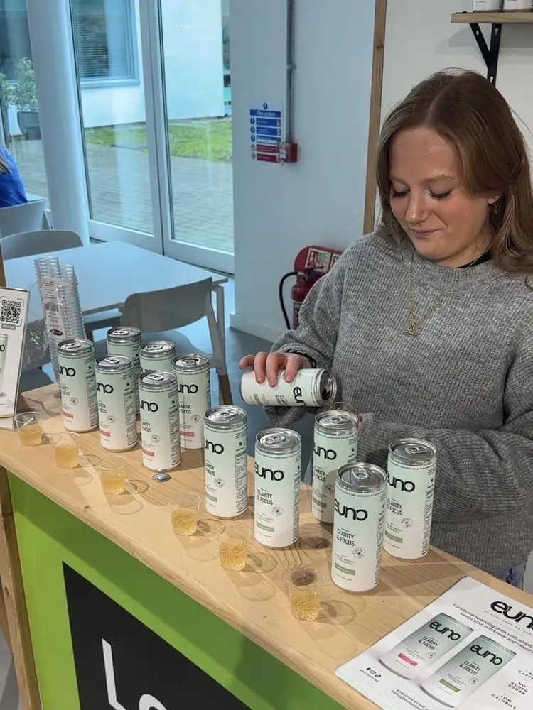Pouring Euno Clarity & Focus sparkling drink samples into small cups at a sampling stand
