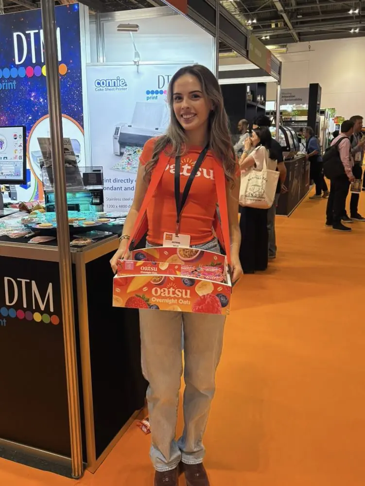 Katrina at a trade show in an orange Oatsu t-shirt holding a tray of Overnight Oats samples